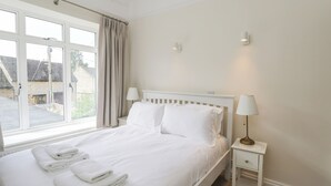Un lit bien fait, avec du linge de lit et des serviettes blanches, une table de chevet avec une lampe et une fenêtre avec des rideaux.