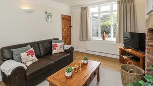 Un salon avec un canapé en cuir marron, une table basse en bois ornée de plantes, un téléviseur posé sur un meuble en bois et une fenêtre avec des rideaux.