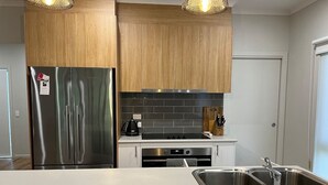 Una cocina moderna con electrodomésticos de acero inoxidable, armarios de madera, salpicadero de azulejos negros y un lavabo doble.