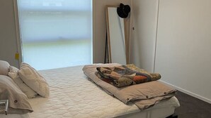 Un dormitorio con cama, mesita de noche, espejo y ventana con persianas.