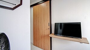 Une pièce avec une armoire en bois, un téléviseur à écran plat posé sur une étagère en bois et un ventilateur de plafond.