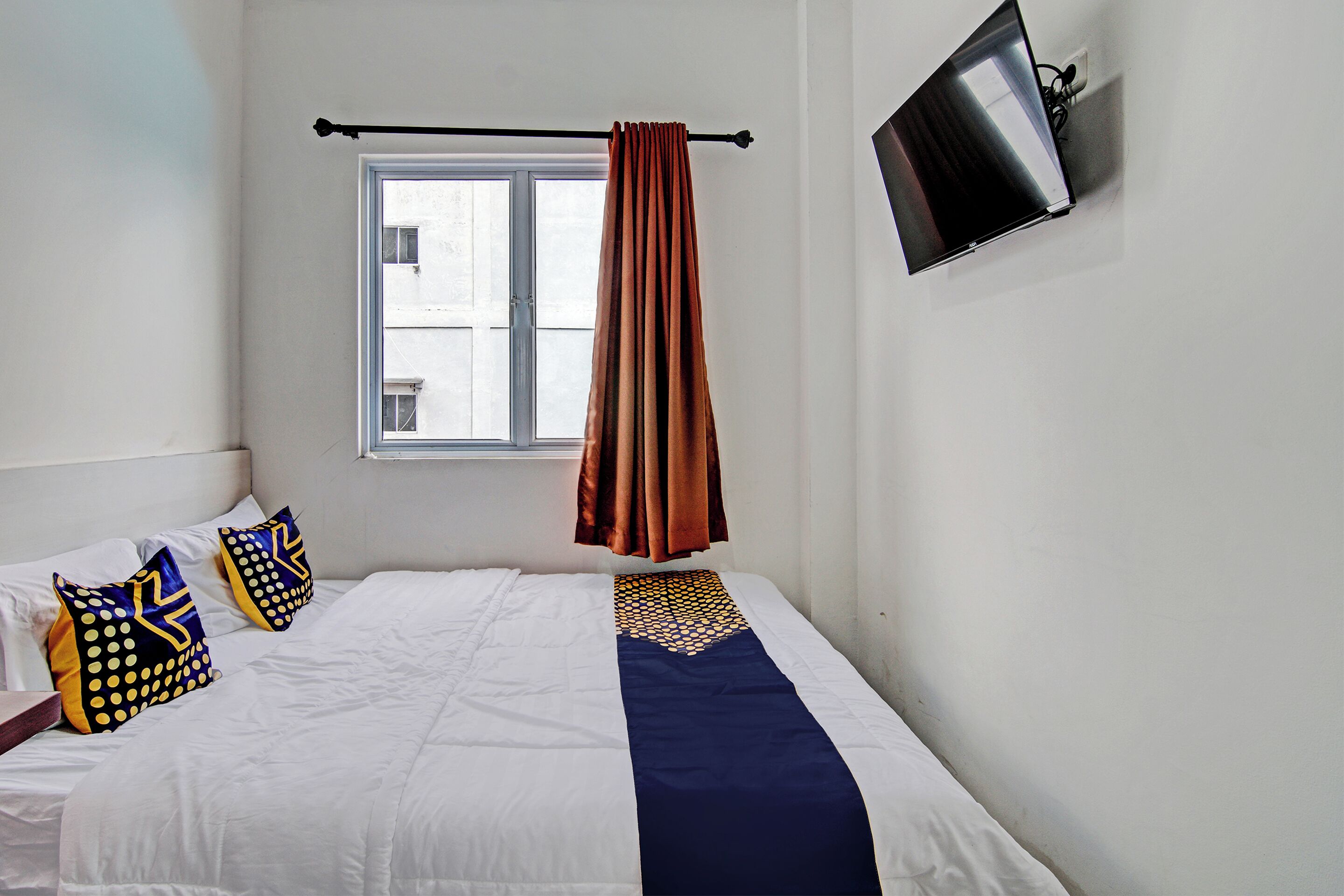 A hotel room with a bed, a window, a TV mounted on the wall, and a curtain.