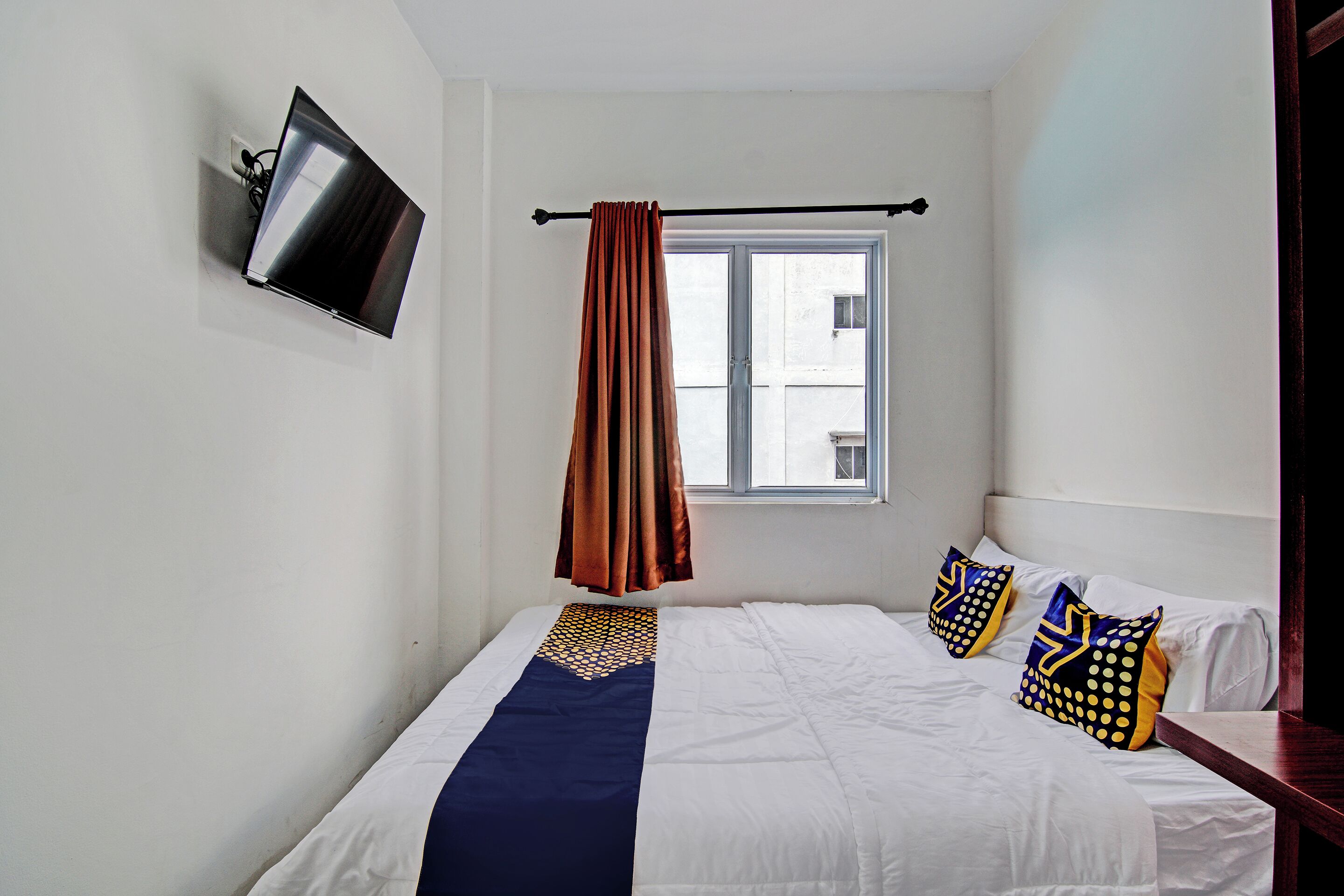 Ein Hotelzimmer mit Bett, Wandfernseher, einem Fenster mit Vorhängen und Blick ins Freie.