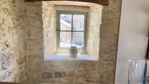 Une pièce aux murs de pierre, avec une petite fenêtre et une poutre en bois au-dessus.