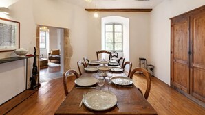 Un coin repas avec une table en bois dressée pour six personnes, entourée de chaises en bois, et une fenêtre qui laisse entrer la lumière naturelle.
