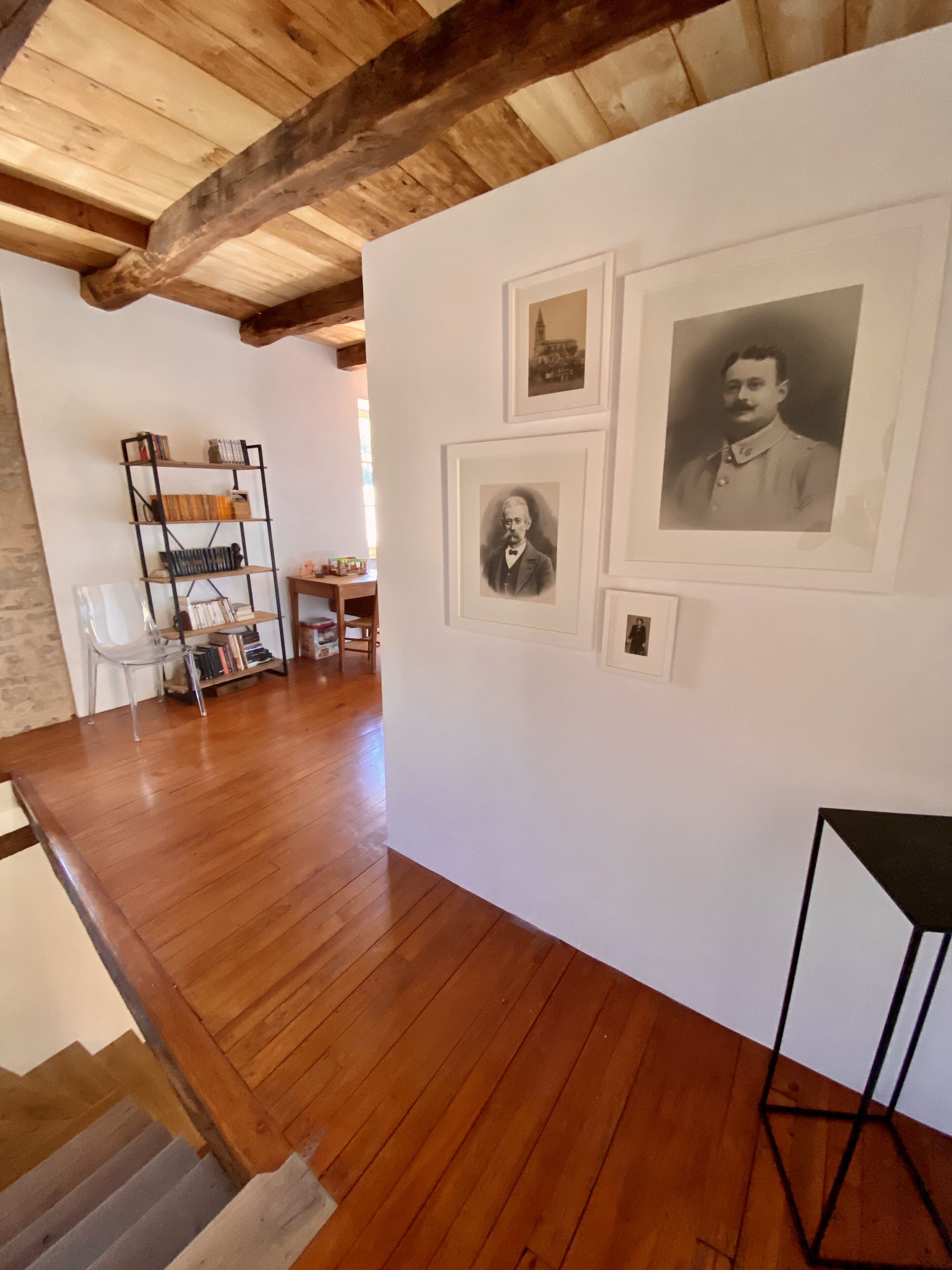 Une pièce avec un plancher en bois, une bibliothèque et des portraits encadrés accrochés au mur.