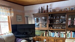 Ein Wohnzimmer mit einer Couch, einem Glastisch, einem Fernseher und einem Bücherregal voller Bücher und Dekoration.