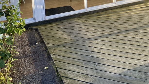 Eine überdachte Terrasse mit Tisch und Stühlen, ein Holzboden und eine Glastür, die zu einem Zimmer mit einem Bett und einem Fenster führt.