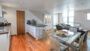 A spacious kitchen with a central island, a dining area with a glass table, and a living room with a sofa and TV. - 2 Bed Duplex close to Millennium Sq (Leeds)