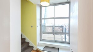 A stairwell with a yellow wall, a window with a view of buildings, and a light fixture above the window. - 2 Bed Duplex close to Millennium Sq (Leeds)