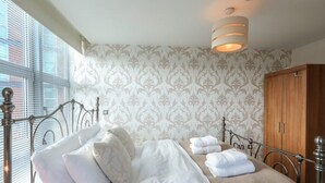 A neatly made bed with white linens and pillows, a wooden wardrobe, and a patterned wallpaper. - 2 Bed Duplex close to Millennium Sq (Leeds)