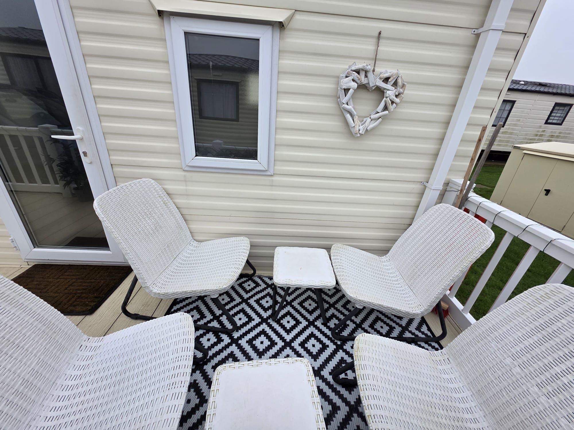 Eine Terrasse mit wei ßen Korbmöbeln, einem gemusterten Teppich und einer weißen Tür mit Fenster.