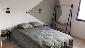 Un dormitorio moderno con una cama, dos mesitas de noche, una silla colgante y un ventanal.