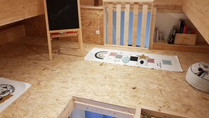 Una habitación de madera con una pizarra, una puerta a rayas azules y blancas, y una mesa con varios documentos.