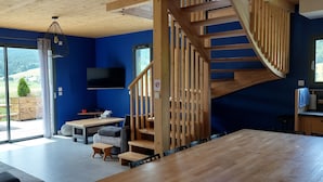 Un interior moderno con una escalera de madera, una zona de comedor y un amplio ventanal con vistas al exterior.