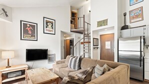 A living room with a sofa, coffee table, TV, and a staircase leading to an upper level. - Conveniently Located in West Keystone with Private Balcony & Gas Fireplace! (Keystone)