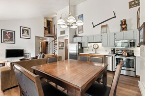 Et moderne køkken med rustfrie hårde hvidevarer, et træspisebord og en trappe til en etage ovenpå.