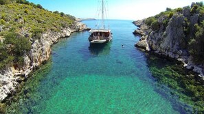 Boat anchored in a tranquil turquoise sea, surrounded by rugged rock formations and lush vegetation.