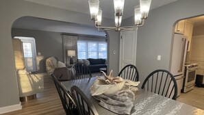 A dining area with a large table, chairs, and a chandelier. There is a sofa and a window in the background. - The Warm & Inviting Place (Sioux Falls)