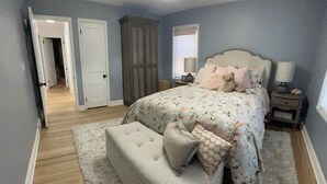 A bedroom with a bed, a bench, a nightstand, a lamp, and a door leading to another room. - The Warm & Inviting Place (Sioux Falls)