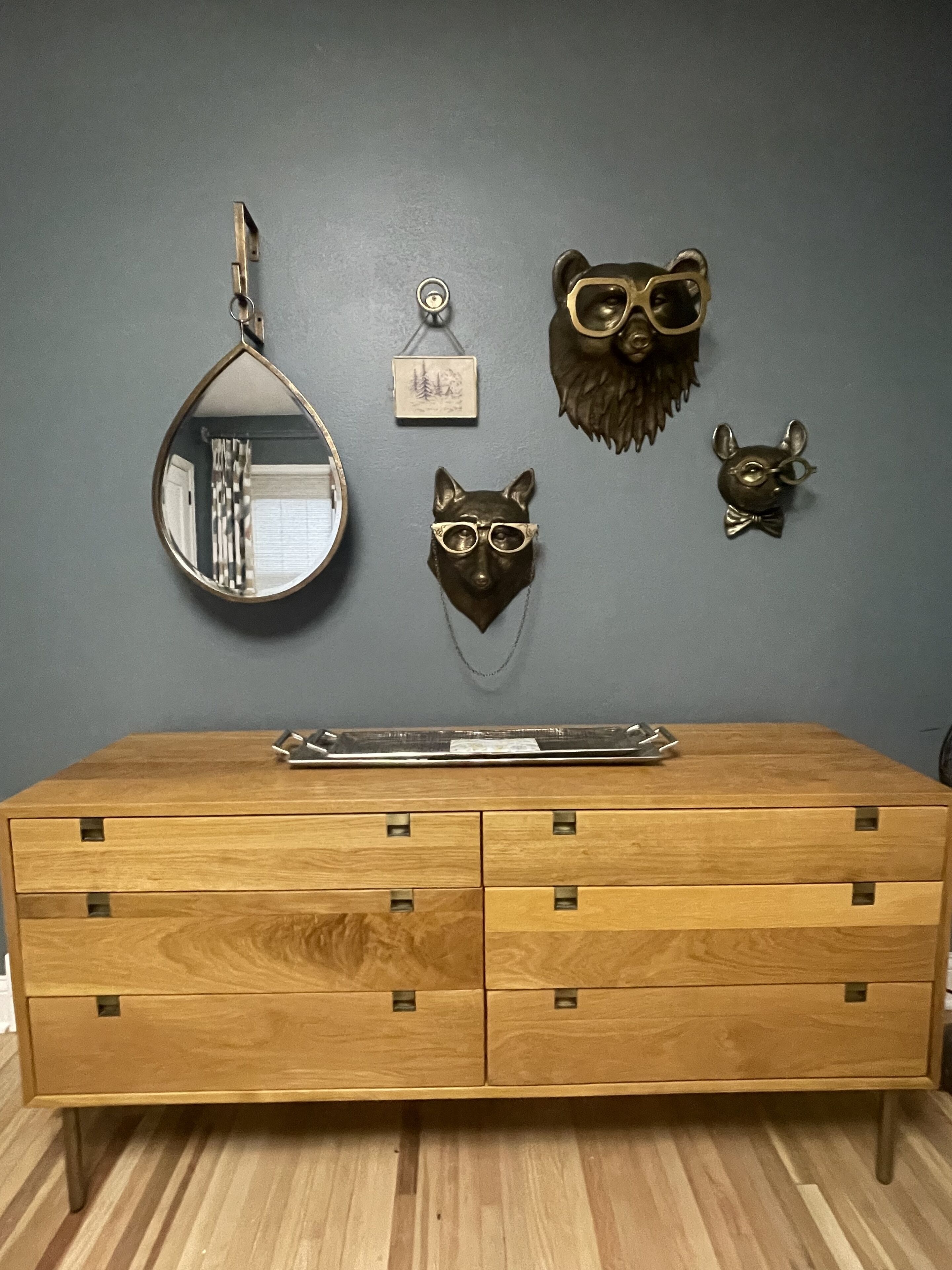 Un aparador de madera con un espejo, un pequeño marco de fotos y tres adornos con motivos de osos.