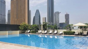 Una piscina en la azotea con sillones de descanso y el horizonte de la ciudad al fondo.
