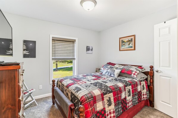 A bedroom with a bed, a dresser, a window with blinds, and a door.