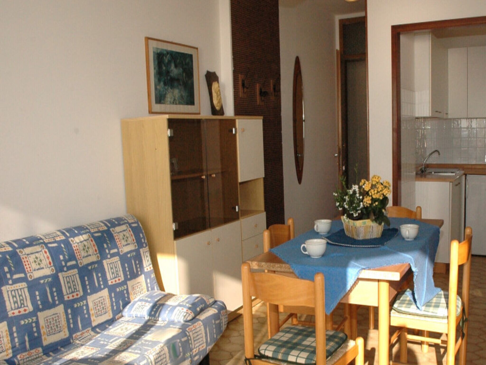 Ein kleiner, gemütlicher Wohnbereich mit einer gemusterten Couch, einem Holzespeisesaal mit blauer Tischdecke und einer Küchenzeile mit Spüle und Schränken.