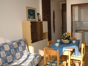 A compact living space with a sofa, dining table, chairs, a cabinet, and a kitchen area.