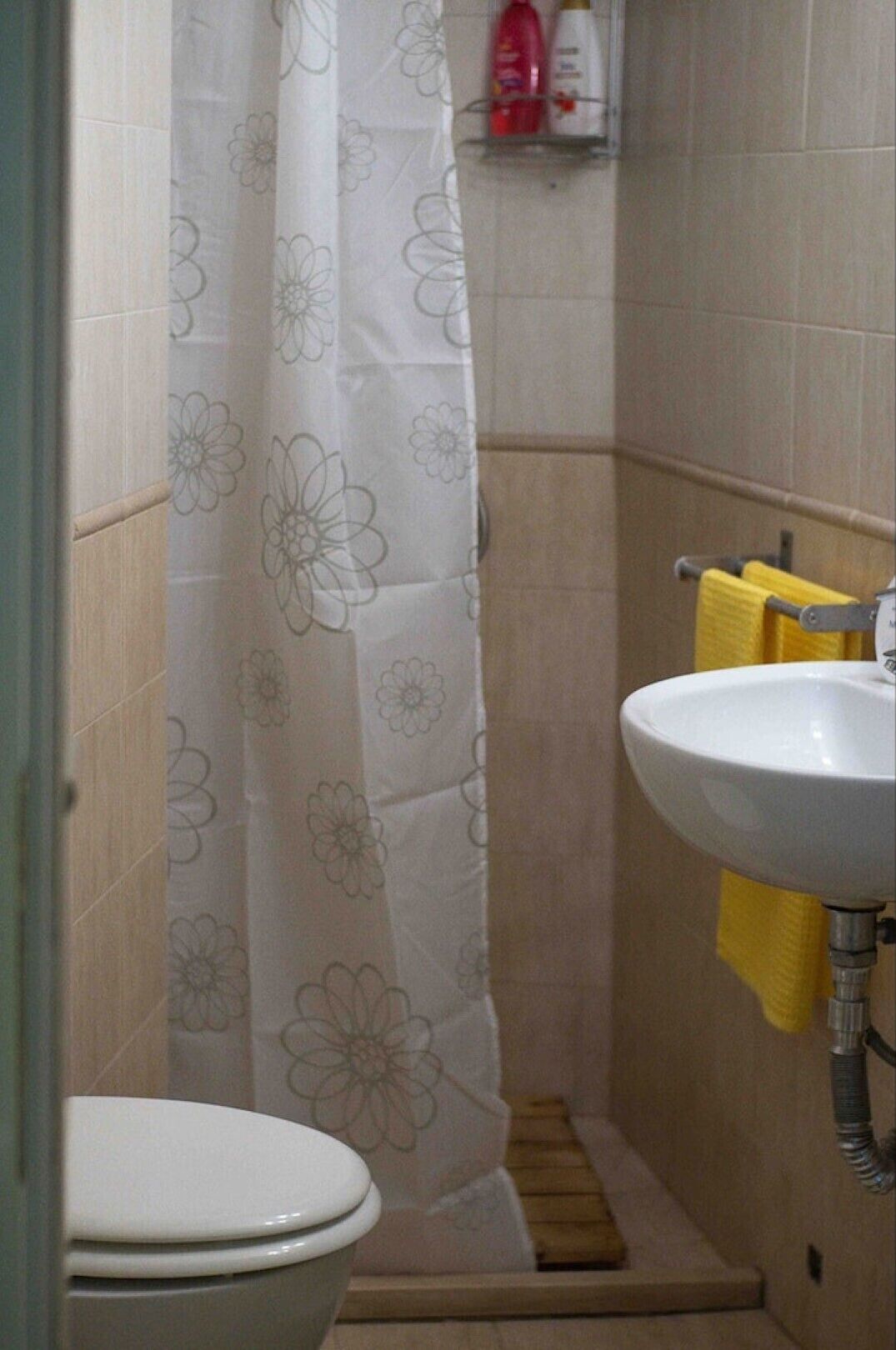 A bathroom with a shower curtain, a toilet, a sink, and a yellow towel hanging on the wall.