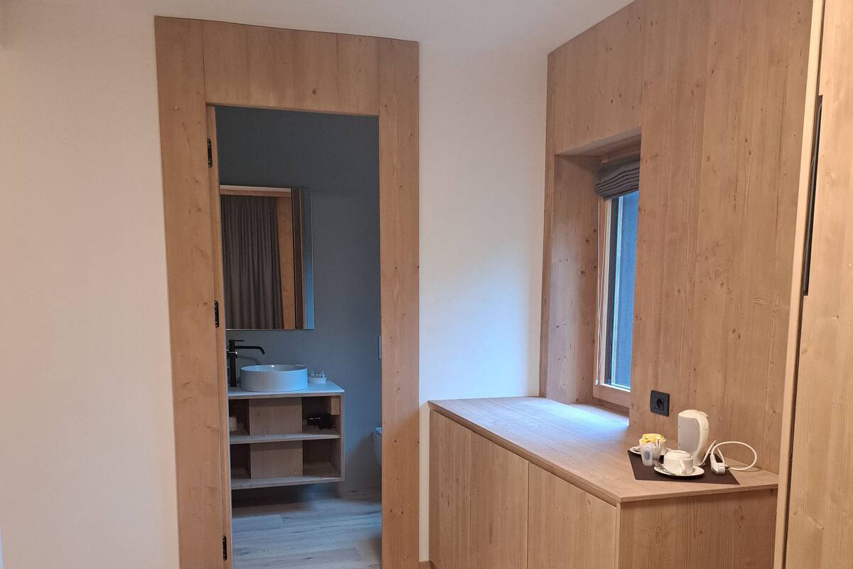 Une pièce de taille modeste dotée d’un plancher en bois, d’un coin cuisine avec un évier et un plan de travail, et d’une fenêtre avec des stores.