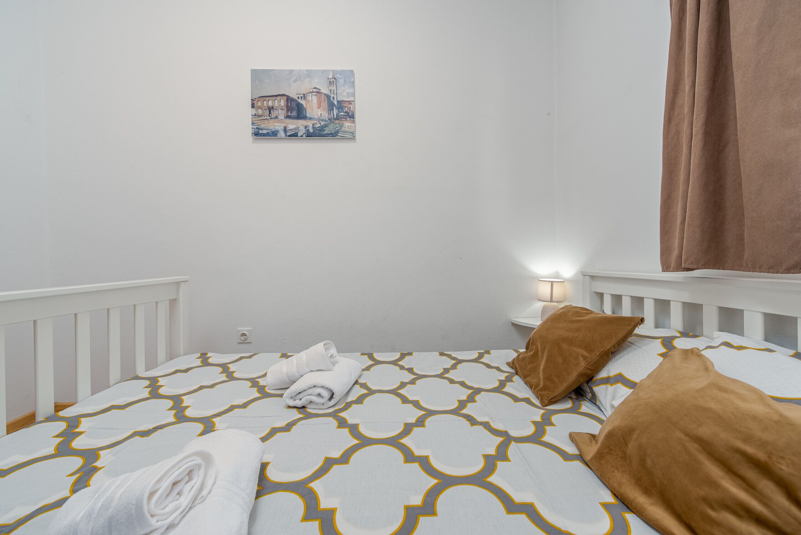 A neatly made bed with a patterned bedspread, a rolled towel, and a pillow.