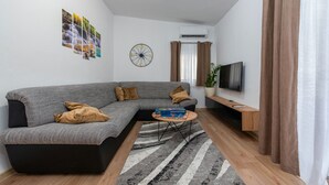 A modern living room with a grey sectional sofa, a round coffee table, a striped rug, a wall clock, a flat-screen TV, and a potted plant. - Villa Luma (Galovac)