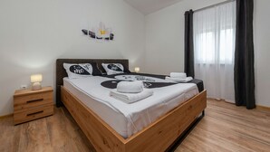 A modern bedroom with a wooden bed, a nightstand with a lamp, and a wall-mounted artwork. - Villa Luma (Galovac)