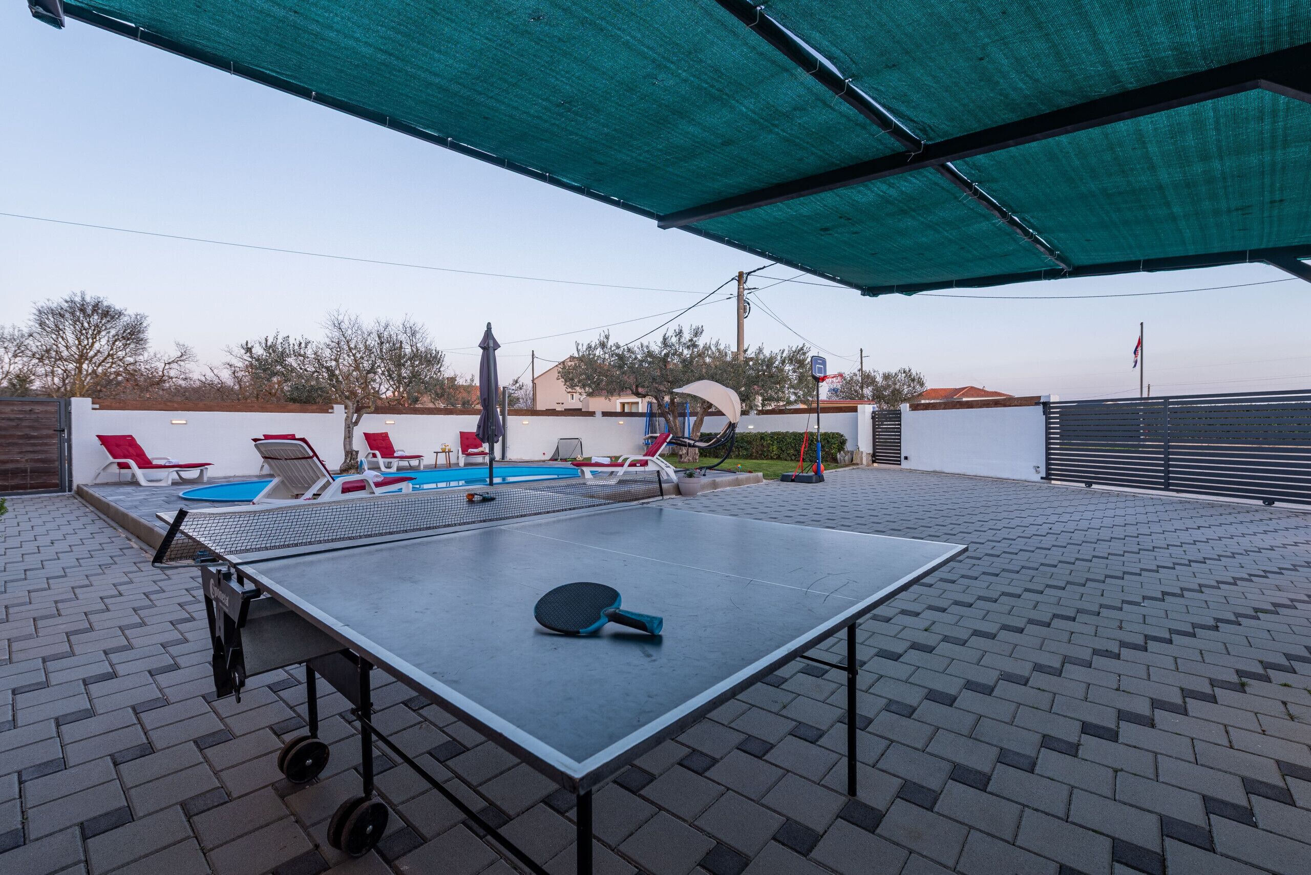 Et udendørs bordtennisbord med net, omgivet af en belagt patio.