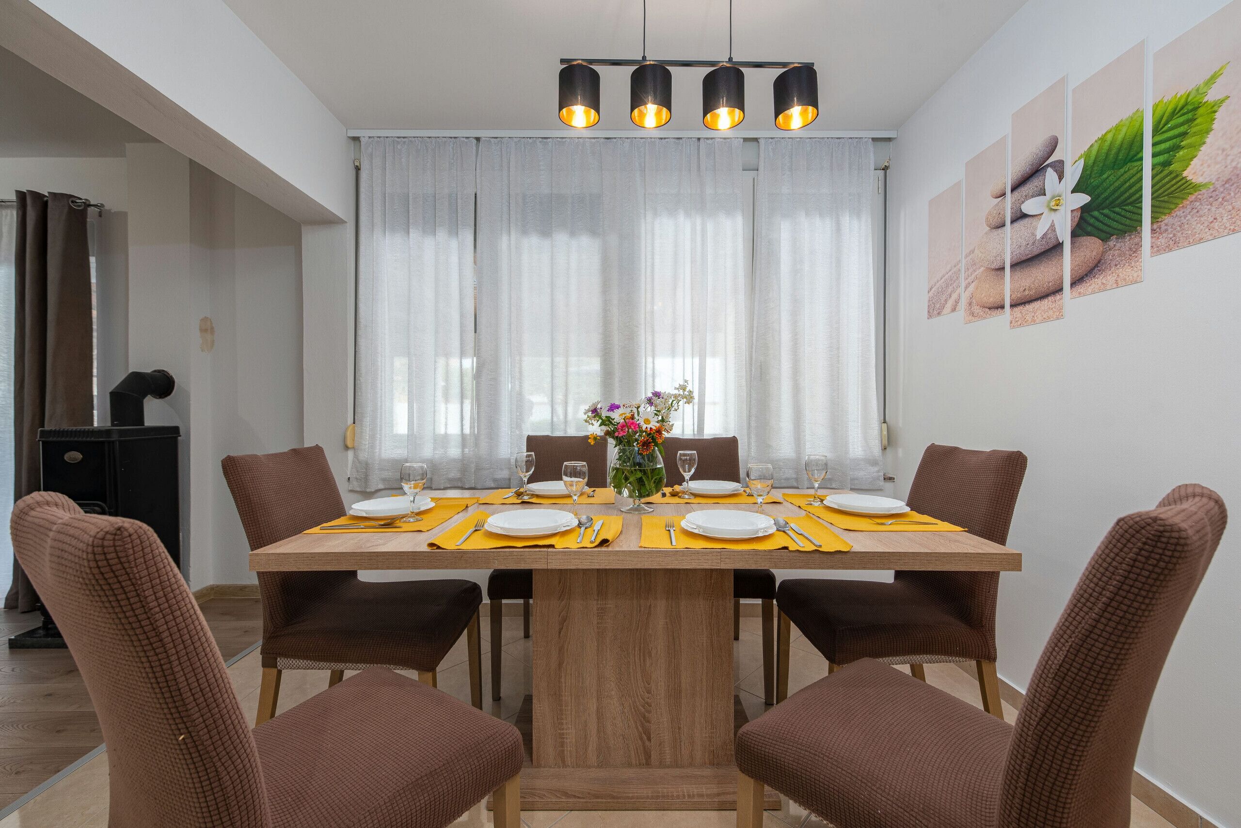 A dining area with a wooden table set for four, surrounded by brown chairs, with a vase of flowers on the table.
