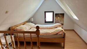 A bedroom with a sloped ceiling, a wooden bed, a nightstand, and a window with blinds. - Anklam Stolpe near Anklam (Stolpe an der Peene)