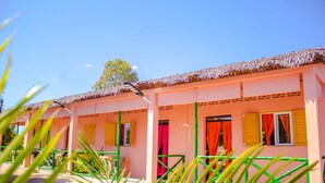 Un edificio rosa con techo de paja, barandillas verdes y cortinas rojas.