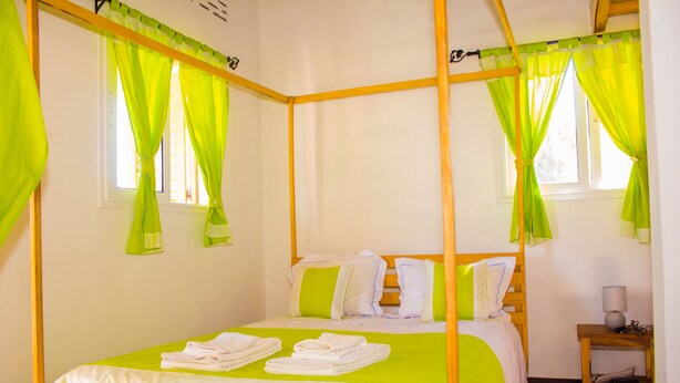 Una cama con dosel adornada con cortinas verdes, ropa de cama blanca y una mesita de noche de madera con una lámpara.