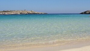 En strand med krystalklart turkis vand, en sandstrand og klippeformationer i baggrunden.