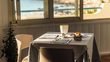 A table set for two with a view of the sea through large windows.