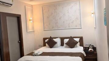 A hotel room with a bed, a ceiling fan, a wall-mounted air conditioner, and a nightstand with a lamp.