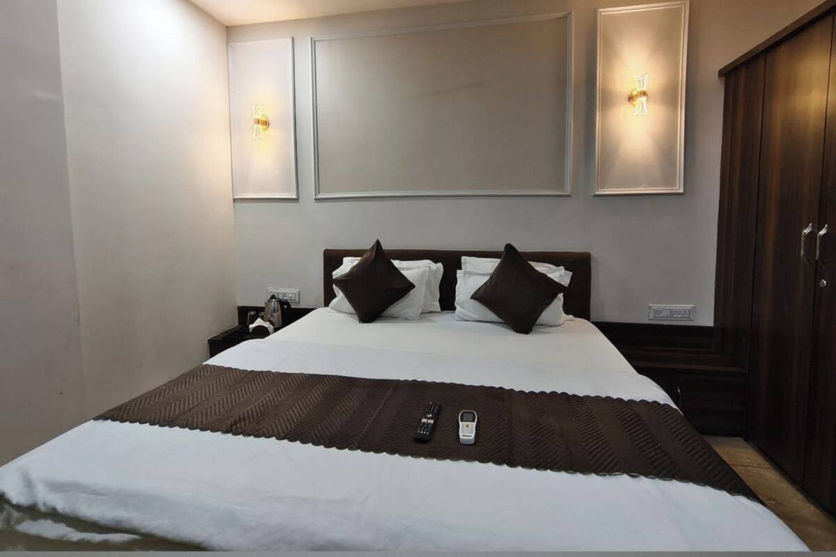 Quarto de hotel com uma cama grande, duas mesas de cabeceira, um guarda-roupa e luzes fixadas na parede.