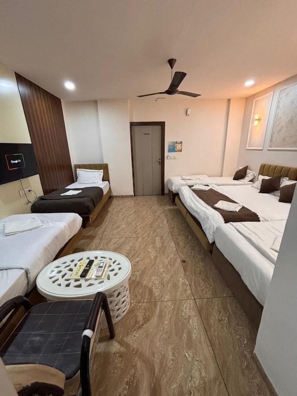 A hotel room with two single beds, a small round table, a chair, a ceiling fan, and a TV mounted on the wall.