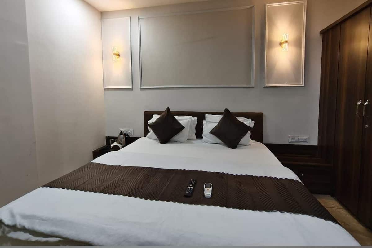 Quarto de hotel com uma cama grande, duas mesas de cabeceira, um guarda-roupa e iluminação embutida na parede.