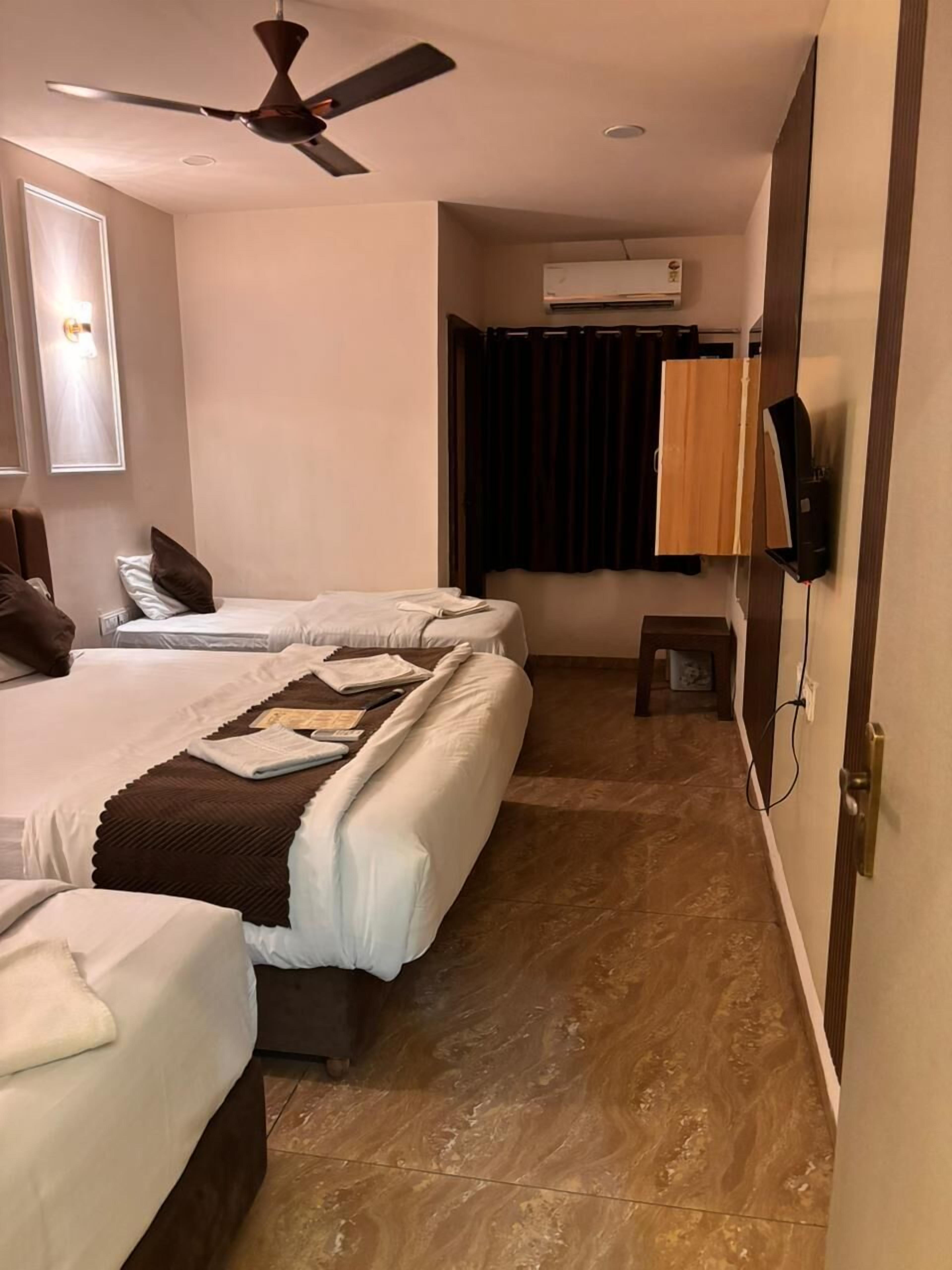 Habitación de hotel con dos camas, ventilador de techo, aire acondicionado, televisor y una mesita pequeña.