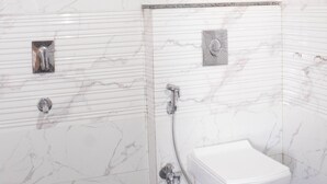 Une salle de bain aux murs recouverts de marbre blanc, avec une douche et des toilettes.