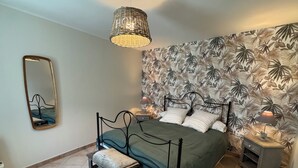 Een slaapkamer met een bed, nachtkastje, lamp, bankje, hanglamp en spiegel.