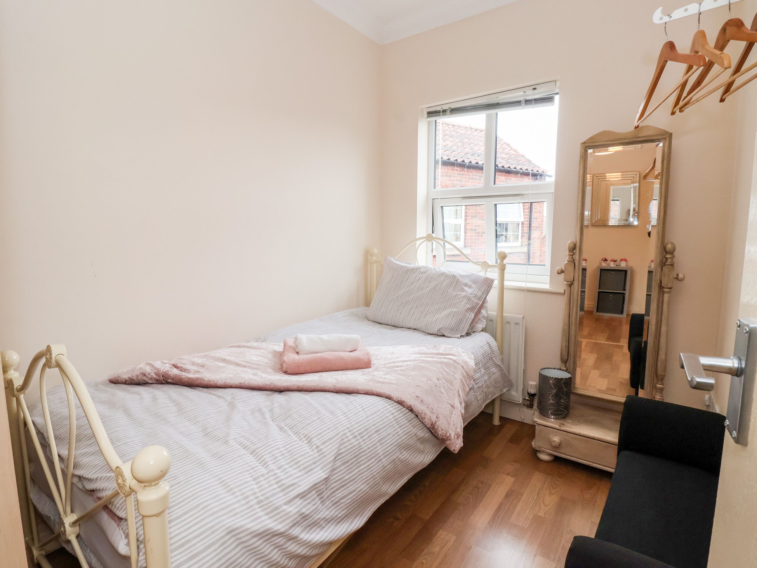 Un dormitorio pequeño y ordenado con una cama individual, una ventana, un espejo y una mesita de noche.
