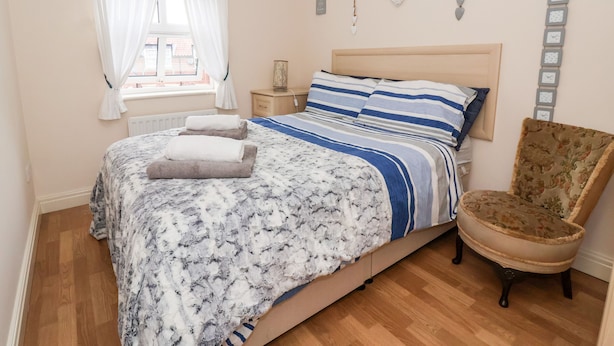 Un dormitorio con cama, una silla, una mesita de noche y una ventana con cortinas.